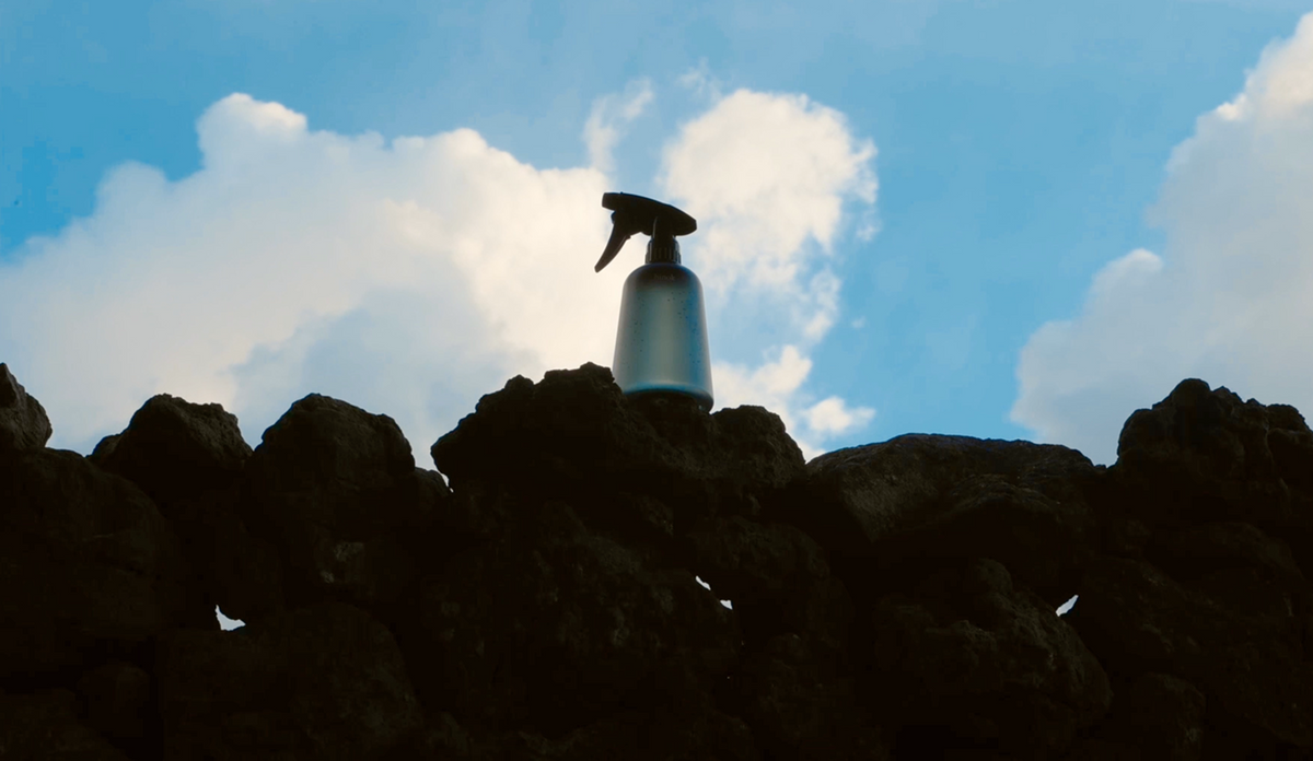Spray bottle on volcanic rocks under blue sky, evoking natural wellness and mindful living rituals.