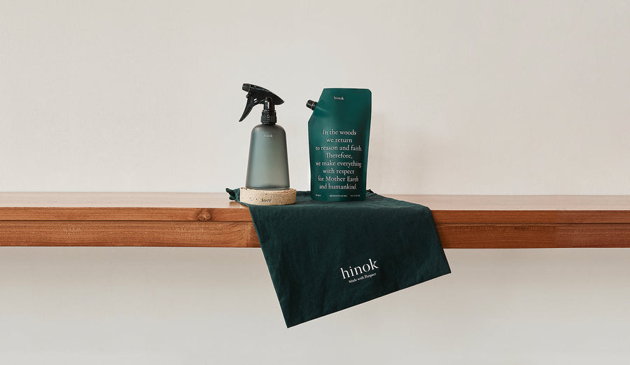Hinok spray bottle and refill pouch on wooden shelf with branded cloth, promoting mindful living and respect for nature.