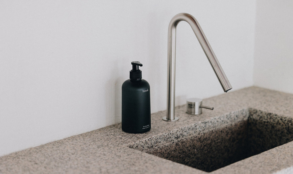 Black hinok hand wash bottle beside modern faucet on stone countertop, minimalist bathroom aesthetic