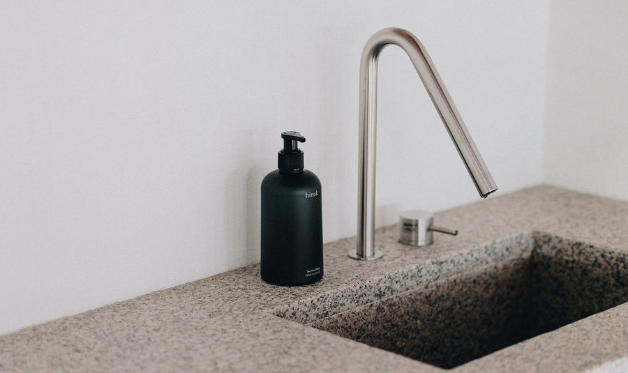 Black hinok hand wash bottle beside modern faucet on stone countertop, minimalist bathroom aesthetic