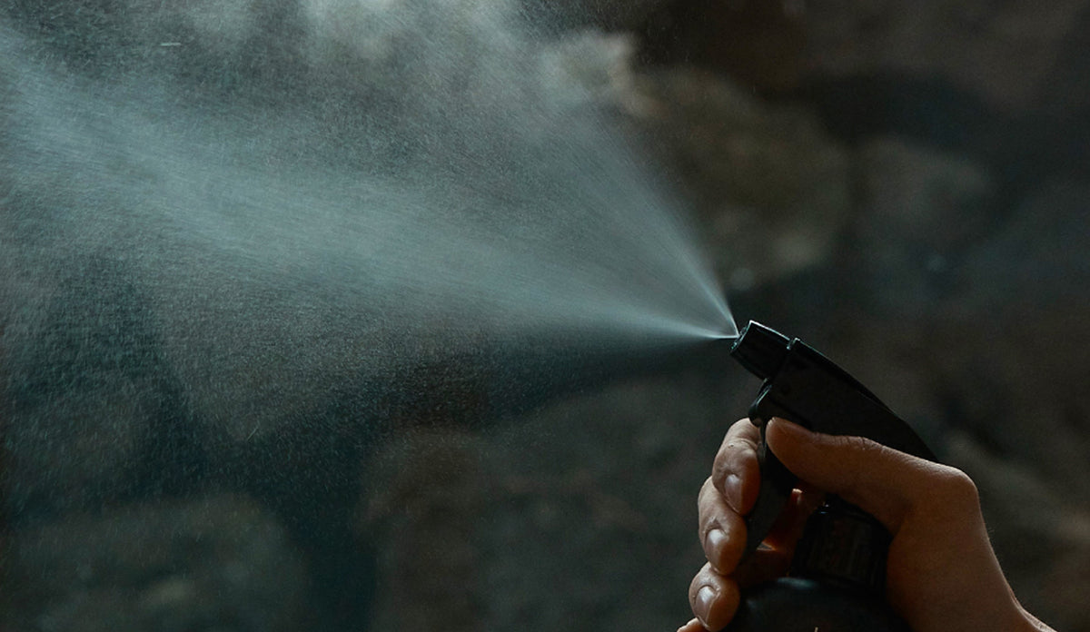 Hand spraying fine mist from black bottle, evoking mindful ritual with natural cypress essence