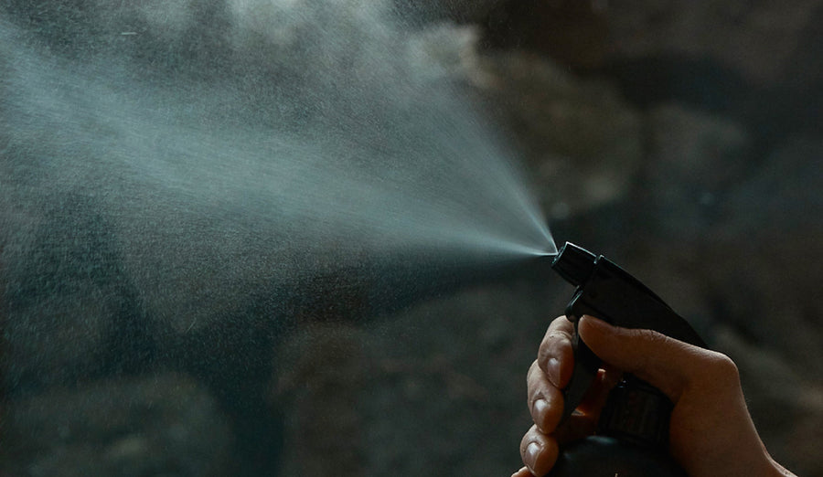 Hand spraying fine mist from black bottle, evoking mindful ritual with natural cypress essence