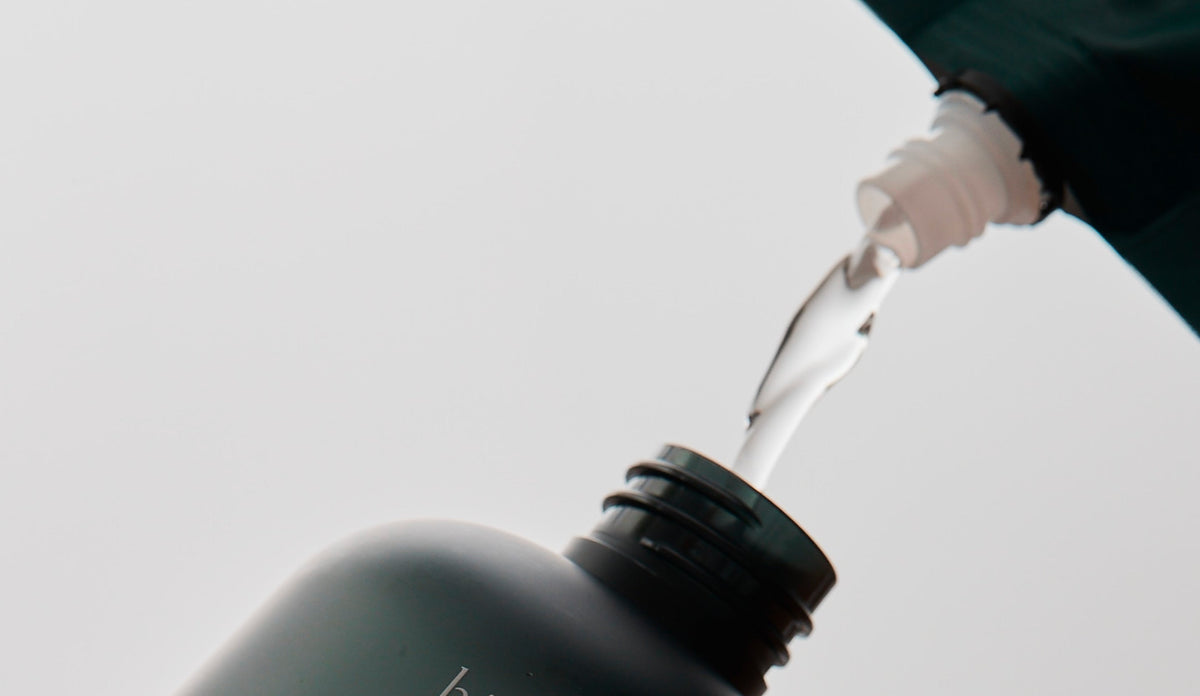 White liquid pouring from dark bottle, mindful skincare ritual with Jeju Hinoki Cypress essence