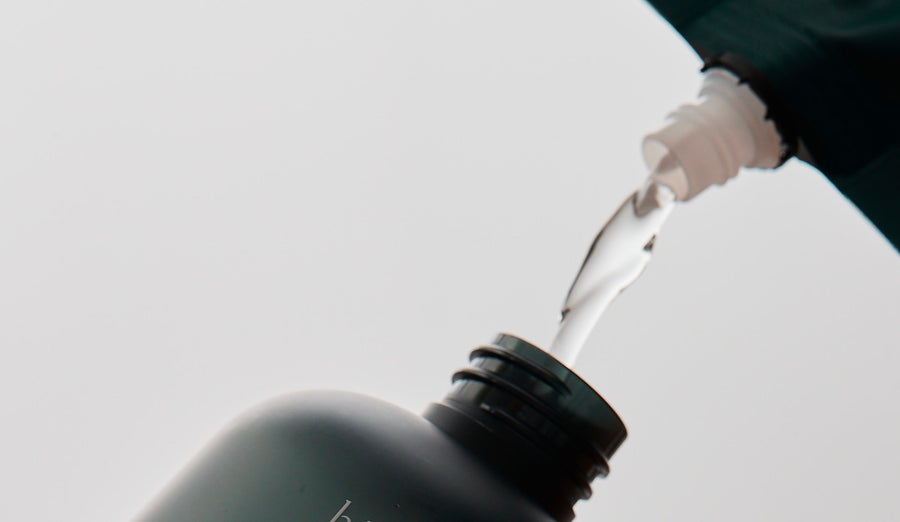 White liquid pouring from dark bottle, mindful skincare ritual with Jeju Hinoki Cypress essence