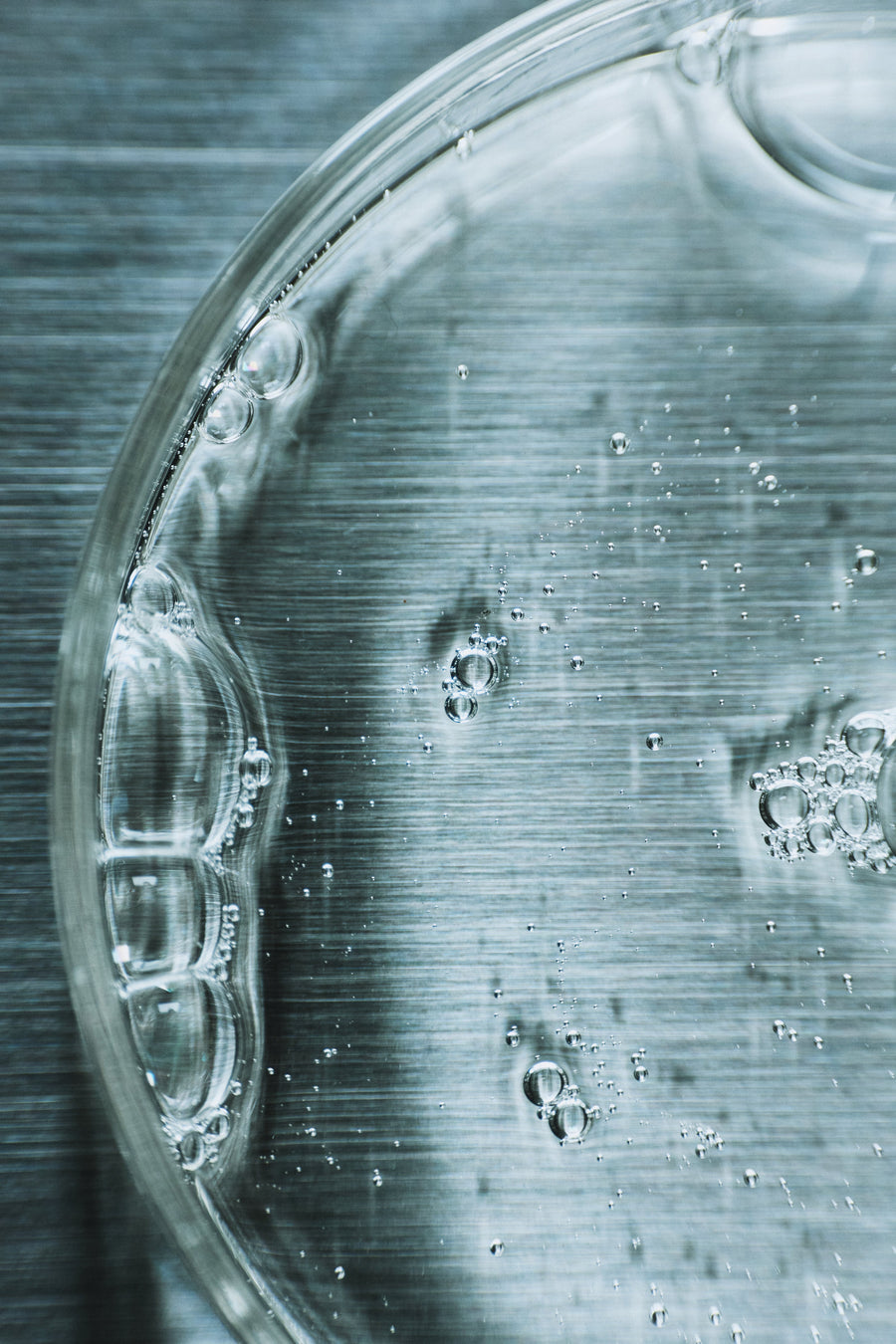 Clear glass bottle with water droplets and bubbles on brushed metal surface, evoking purity and mindful care.