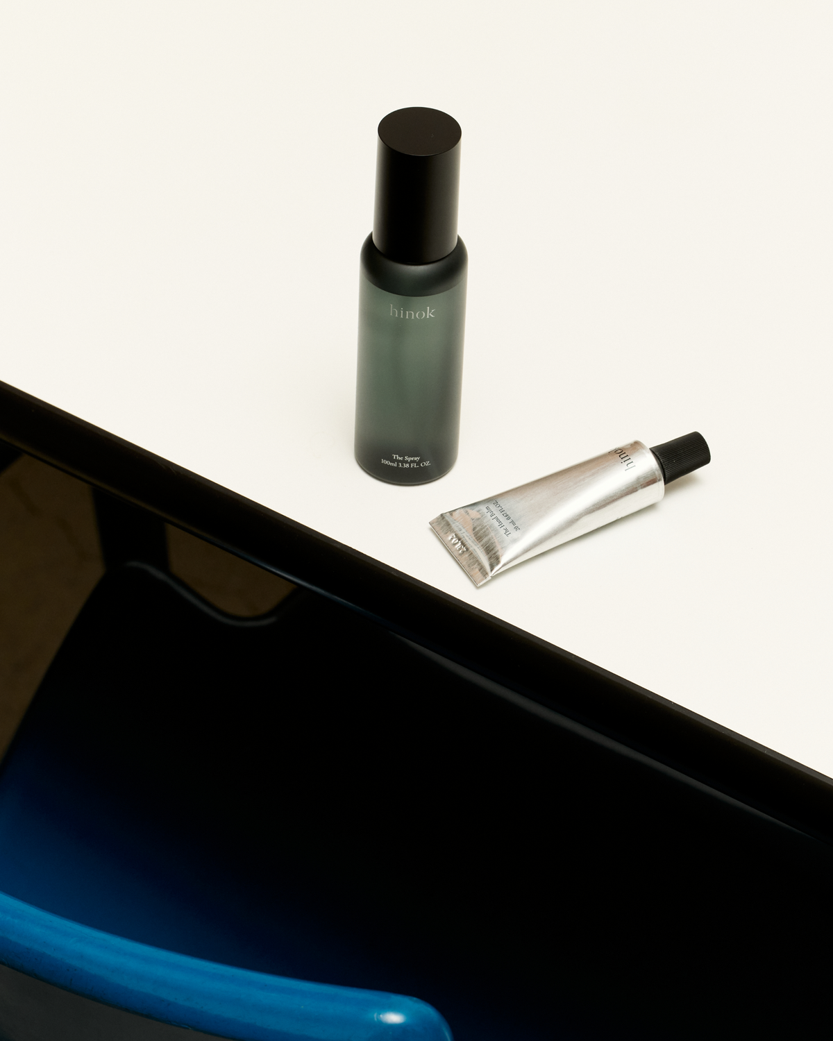 The Spray To Go and The Hand Balm Mini beside a dark tabletop