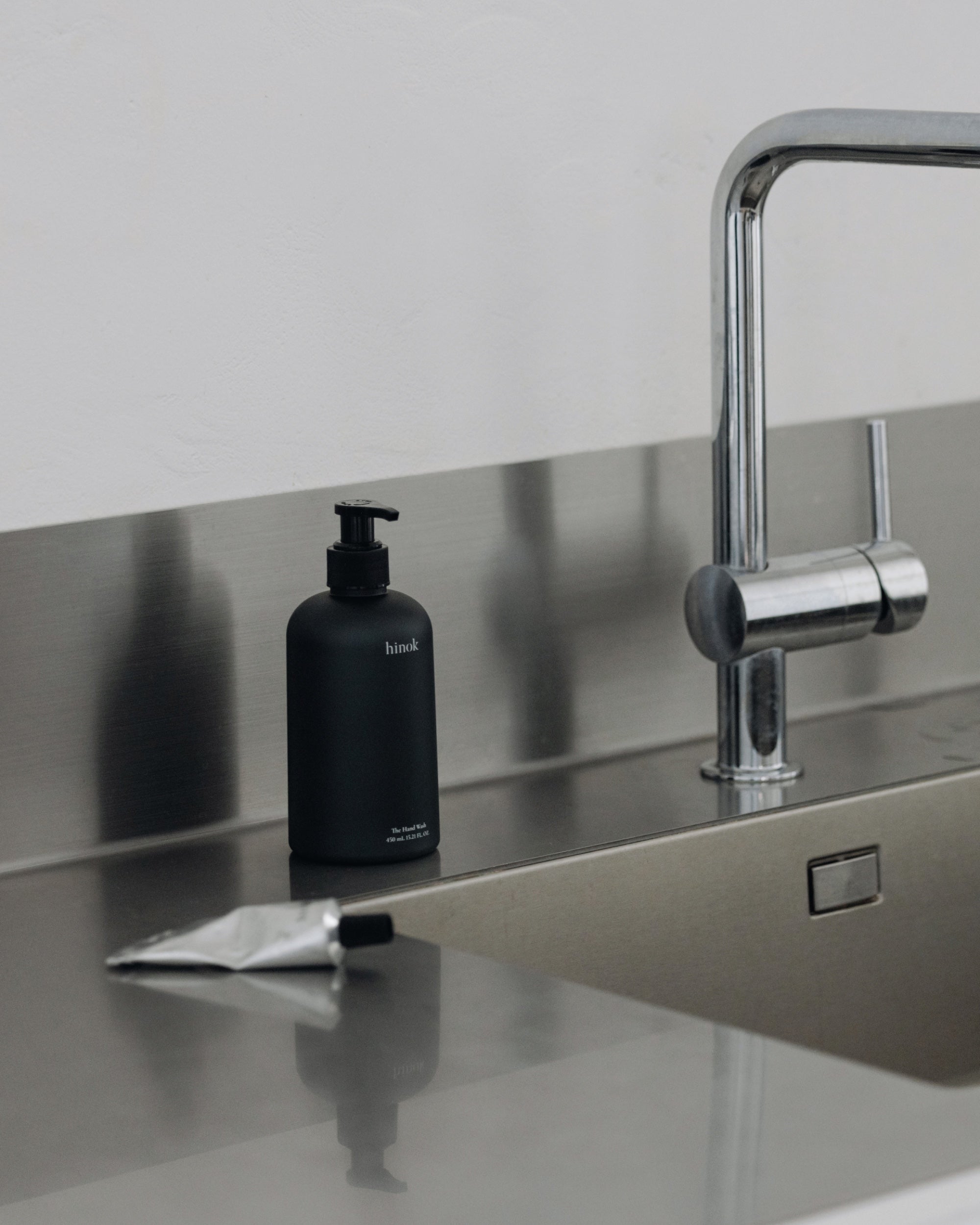 The Hand Wash beside a stainless steel sink with The Hand Balm in the foreground